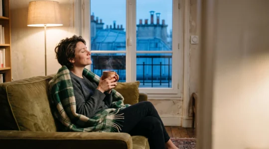 Personne installée confortablement sous un plaid dans un salon français chaleureux, illustrant la sobriété énergétique sans perte de confort