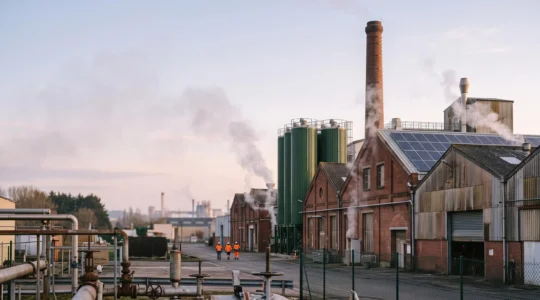 Site industriel français en pleine transition énergétique, chaudière biomasse et panneaux solaires coexistant avec les lignes de production actives